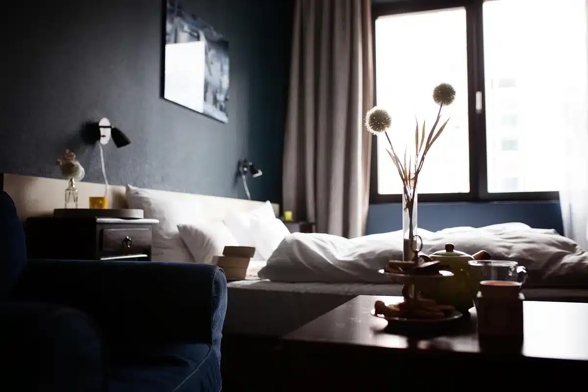 An empty hospital bed with a folded blanket and an unused pair of compression stockings on the bedside chair, a dim corridor beyond the doorway