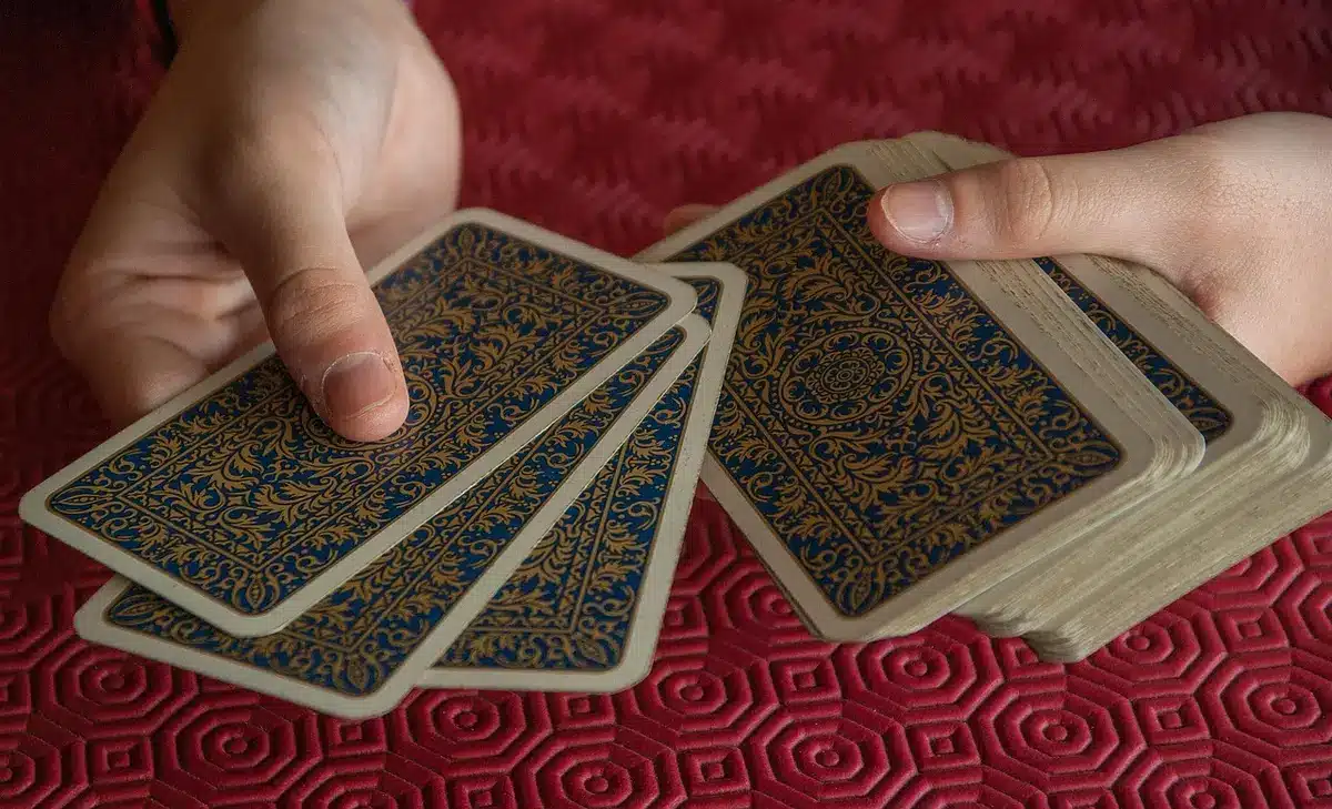 A single anonymous pair of hands holding a folded, worn playing card marked with a spade symbol on plain cloth, light falling across the card, no faces visible