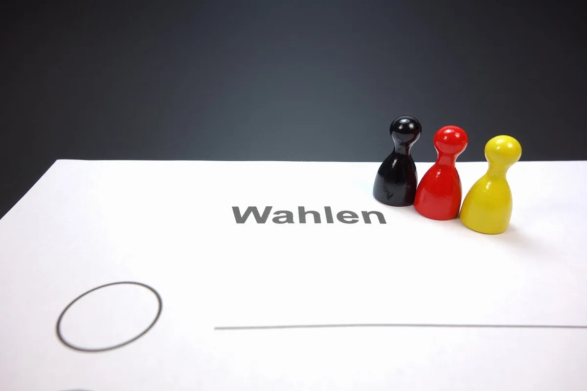A close-up of stacked absentee ballots and a generic voter guide on a table, no identifying marks — a symbolic image of voting mechanics