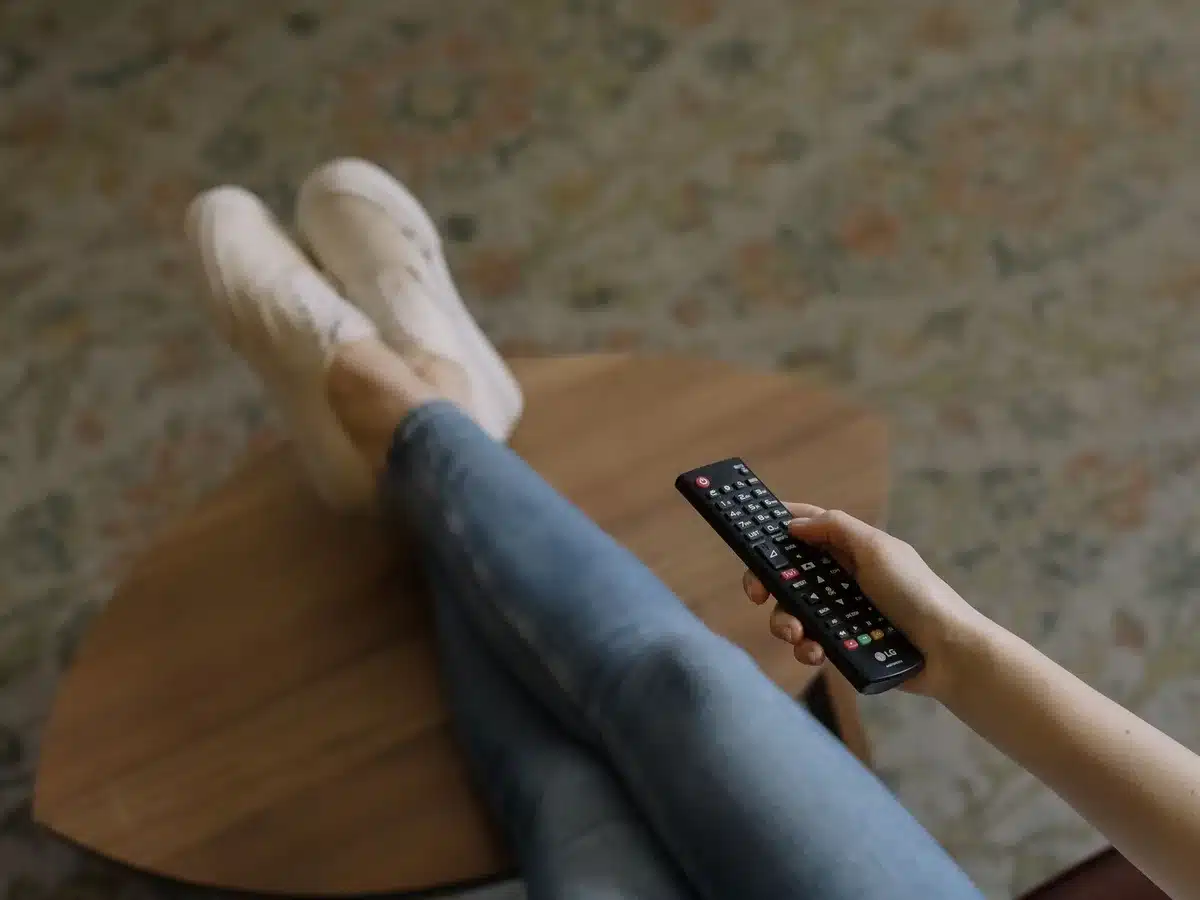 A turned-off living room TV with a paused, anonymous campaign ad frame on screen, a remote control on a coffee table in the foreground, empty chairs and a stack of mail nearby