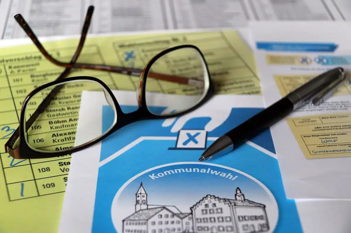 A clean desktop with a laptop showing a detailed election-results dashboard map, a notepad with scribbled county names beside it, and a pen — no logos or identifiable screens