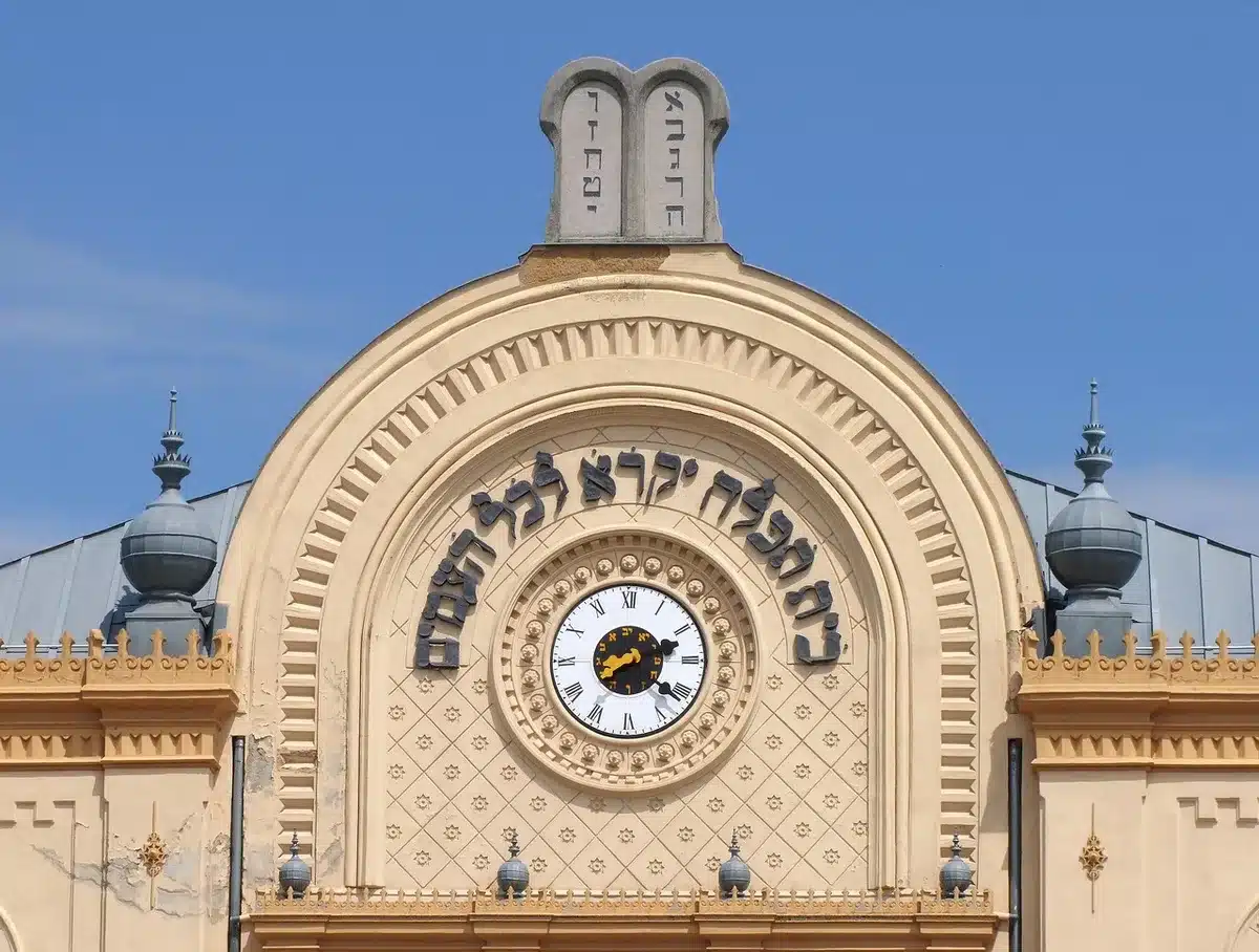 Empty synagogue exterior with locked doors and generic security fencing, evening lighting, a lone posted notice on a pole — anonymous civic scene